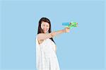 Happy young woman aiming with a toy gun over blue background