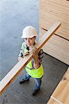 High angle view of female worker carrying wooden plank on shoulder