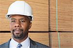 Confident African American male contractor looking away with stacked wooden planks in background