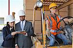 Engineers using tablet PC with female industrial worker driving forklift truck