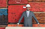 Portrait of happy African American male contractor standing in front of stacked wooden planks