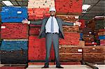 Portrait of happy African American male engineer standing with arms outstretched in front of stacked wooden planks