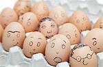 Various facial expressions painted on brown eggs in egg carton