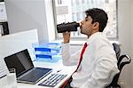 Side view of an Indian businessman drinking water at office desk