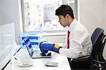 Jeune homme d'affaires indien avec des gants de boxe tout en utilisant un ordinateur portable au bureau