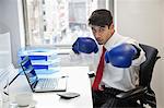 Young Indian businessman wearing boxing gloves at office desk