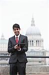 Portrait of a happy Indian businessman using tablet PC against St. Paul's Cathedral