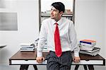 Indian businessman leaning on desk while looking away in office