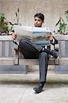 Jeune homme d'affaires indien, lire le journal tout en étant assis sur le banc