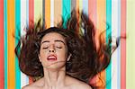 Beautiful young woman tossing hair against colorful striped background
