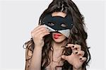 Portrait of sensuous young woman wearing cat mask while biting lip over gray background