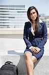 Young Indian businesswoman with bag sitting outdoors