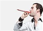 Young man blowing party blower against gray background