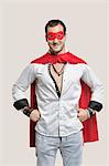 Portrait of young man in superhero costume with hands on hip standing against gray background