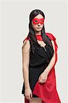 Portrait of young woman in superhero costume standing against gray background