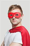 Portrait of young man wearing superhero costume against gray background