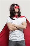 Young man in super hero costume standing with arms crossed against gray background