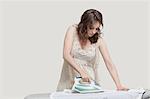 Young woman ironing shirt against gray background