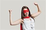 Portrait of a young woman in super hero costume flexing muscles over gray background