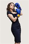 Portrait of a young woman wearing blue boxing gloves against gray background