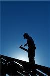 Silhouette de travailleur sur la structure du toit en contre-jour sur fond de ciel bleu profond