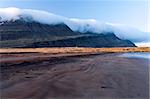 A black sand beach at low tide and mountains in the background, Iceland