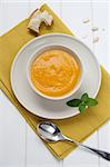 Bowl of pumpkin soup with bread crouton on white wood table