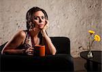 Serious young woman holding coffee mug sitting near table