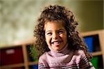 Portraits of children, happy 3 years old female with curly hair smiling and looking at camera in kindergarten