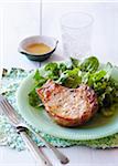 Côtelette de porc et de la salade sur une assiette avec une fourchette et couteau sur napperon