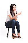 Portrait of beautiful young woman in casuals sitting on stool with mobile phone against white background