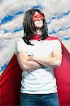 Young man in super hero costume with arms crossed against cloudy sky