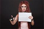 Portrait of arrogant young funky woman pointing towards blank placard against black background