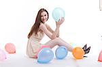 Beautiful young woman in dress on floor with balloons against white background