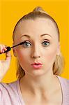 Portrait of a beautiful young woman applying mascara over yellow background