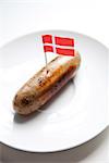 Fried sausage in plate with Danish flag decoration against white background