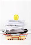 Granny smith apple on stack of documents in desk tray against white wall