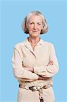 Portrait of smiling senior woman in casuals with arms crossed against blue background