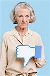 Portrait of senior Woman mit gefälschten Dislike Button vor blauem Hintergrund