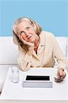 Contemplative woman using cell phone and tablet PC at table