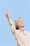 Femme senior en employés occasionnels gesticulant peace sign sur fond bleu