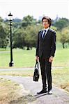 Young businessman carrying briefcase standing at park