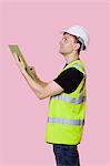 Side view of a male construction worker with clipboard looking away over pink background