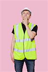 Thoughtful young construction worker looking away over pink background