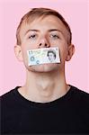 Portrait of a young man with paper money stuck over his mouth against pink background