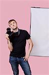 Bored young male photographer holding camera over pink background