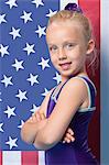 Portrait of a happy young female gymnast with arms crossed standing in front of American flag