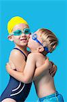 Young siblings in swimwear embracing and kissing over blue background