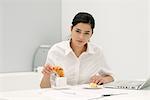 Young woman dipping croissant in coffee at desk in office