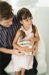 Little girl sitting on father's laps opening present